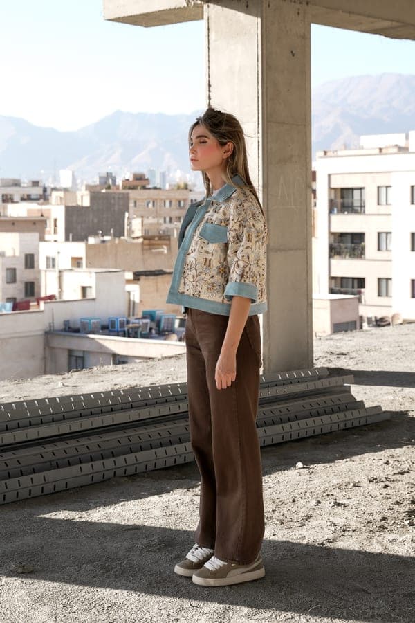 A floral jacket with denim trim and brown trousers, standing on a rooftop above the city