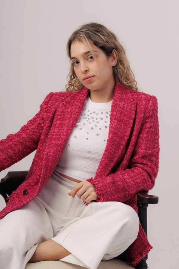 A pink boucle blazer over cream, seated against a plain wall