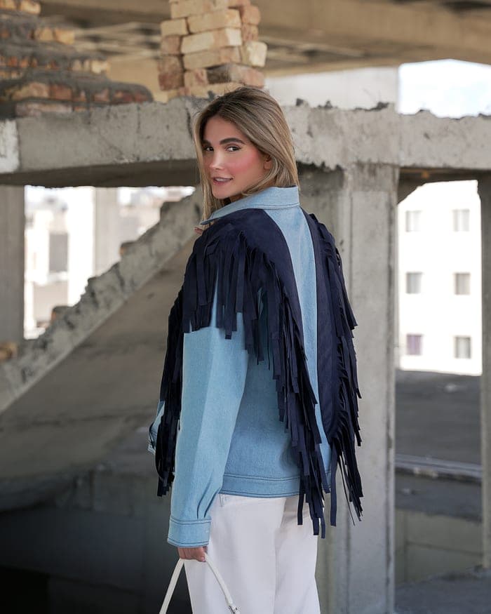 A light denim jacket seen from behind, navy fringe falling from shoulder to hem
