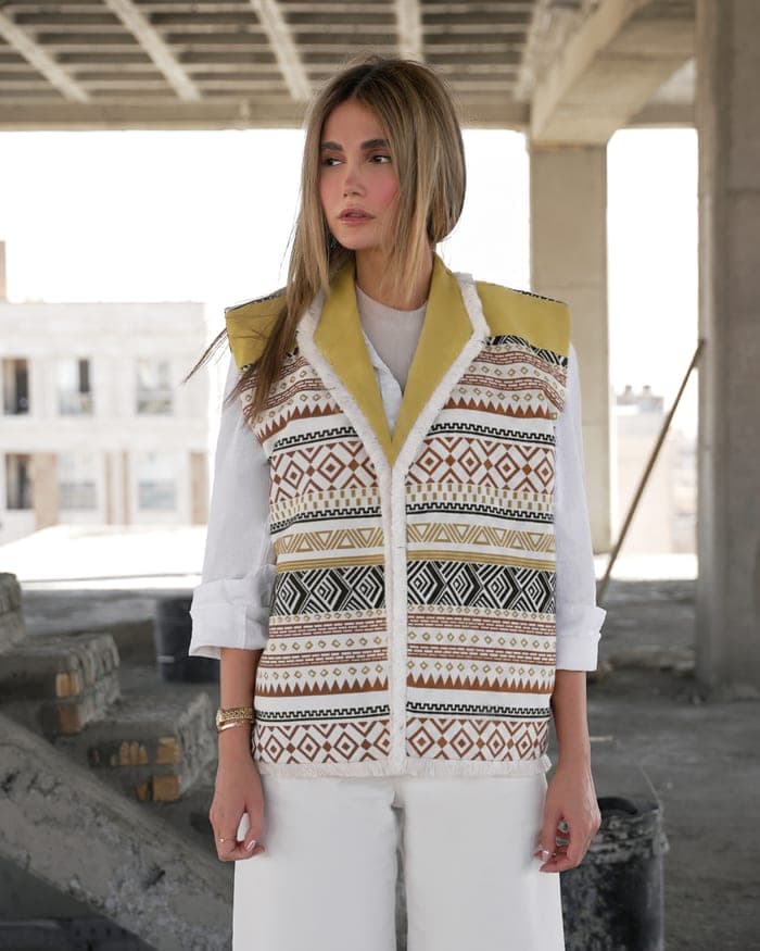 A cream vest patterned in brown, black and ochre, over a white shirt and white trousers