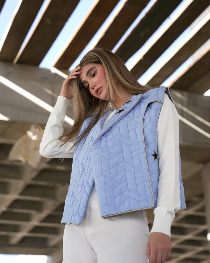A periwinkle quilted vest over a white top, worn open under concrete beams
